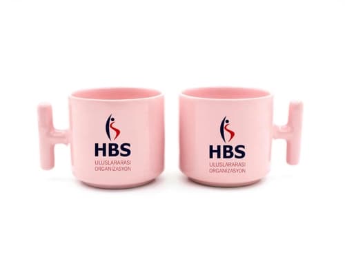 İki pastel pembe promosyon latte fincanı, koyu mavi firma ve organizasyon baskısı