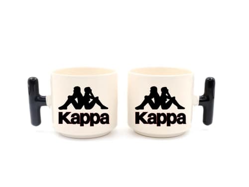 İki beyaz promosyon latte fincanı; siyah kulplu, spor markası logo baskılı